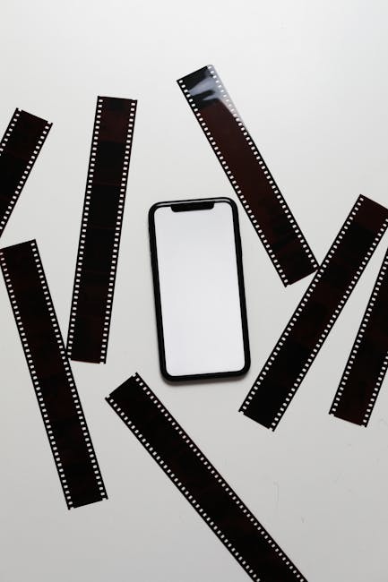 A modern smartphone surrounded by vintage filmstrips, showcasing contrast between digital and analog media.